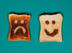 Two slices of toast with happy and sad faces on a teal background.