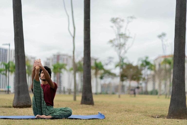 A man doing a yoga stretch on a mat in a serene park, surrounded by trees.