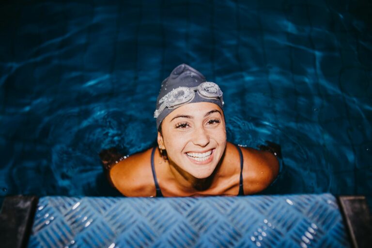 Cheerful woman swimmer in swim cap and goggles enjoying the swimming pool.
