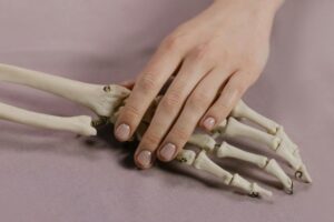 A close-up image of a human hand touching a skeleton hand on a soft background.