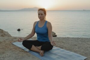 Woman meditating in lotus pose on beach at sunset, serene and peaceful setting.