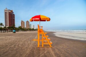 Bright lifeguard tower and umbrella on a tropical beach with city skyline.