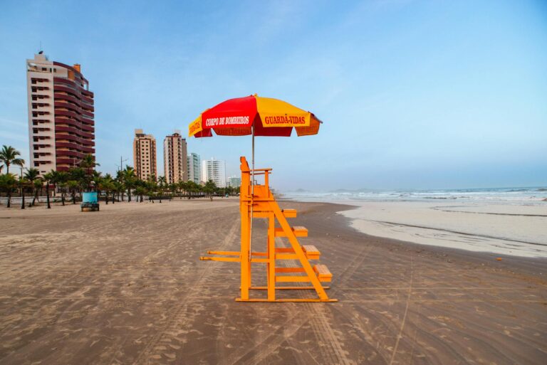 Bright lifeguard tower and umbrella on a tropical beach with city skyline.