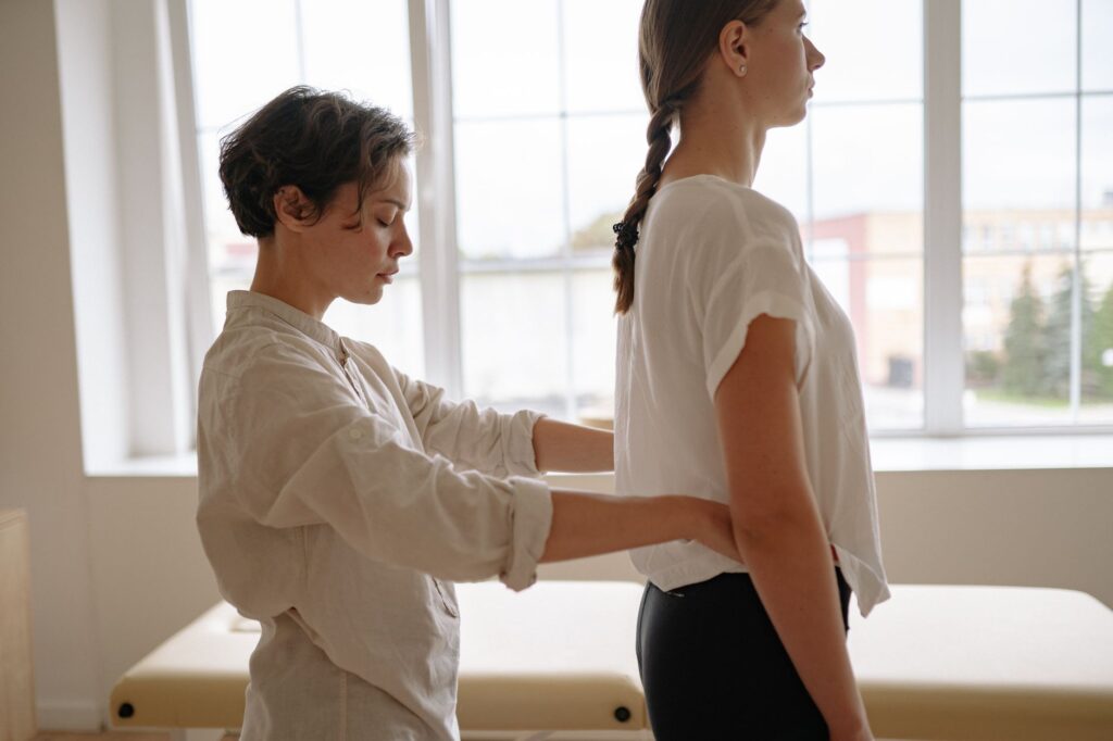 A professional therapist adjusting a standing woman indoors. Ideal for healthcare themes.