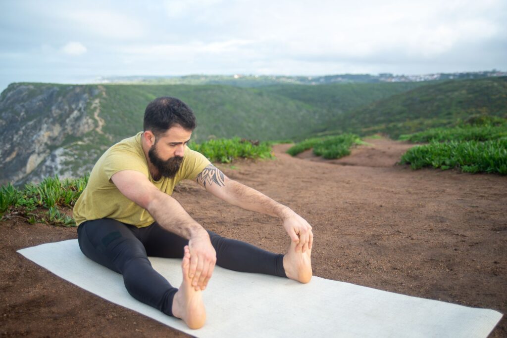 Bearded man stretching on a yoga mat amidst Portugal's scenic landscape, promoting outdoor fitness