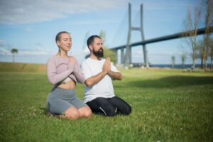 A couple meditating in a grass field near a bridge in Portugal, embracing mindfulness and serenity.