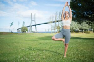 A woman practicing yoga on a grassy field in Lisbon, Portugal, with the Vasco da Gama Bridge in the background.