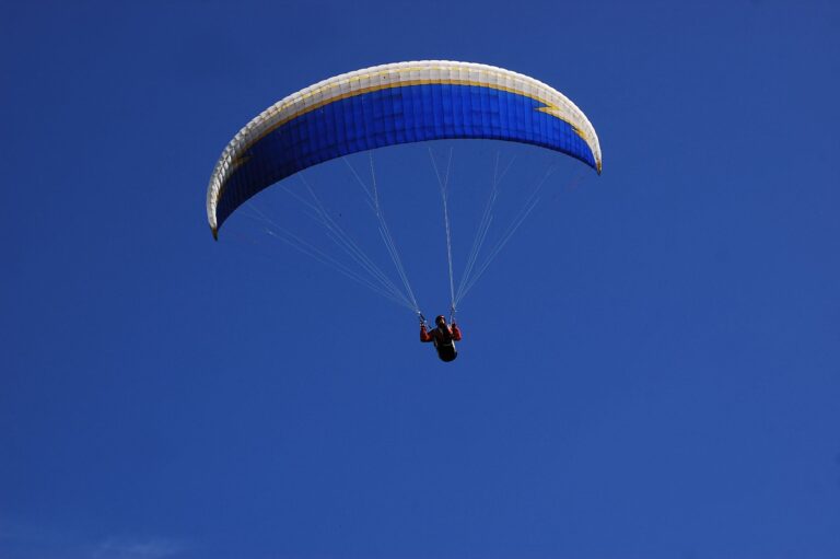 A paraglider sailing through the sky, showcasing adventure sports against a vibrant blue background.