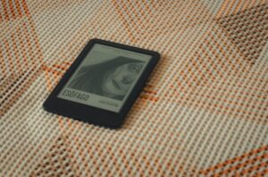 An e-reader displaying a book cover placed on a patterned fabric with warm tones.