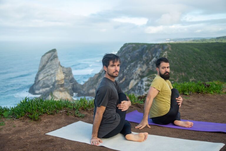 Two men doing yoga on a clifftop in Portugal with scenic ocean views, promoting fitness and relaxation.