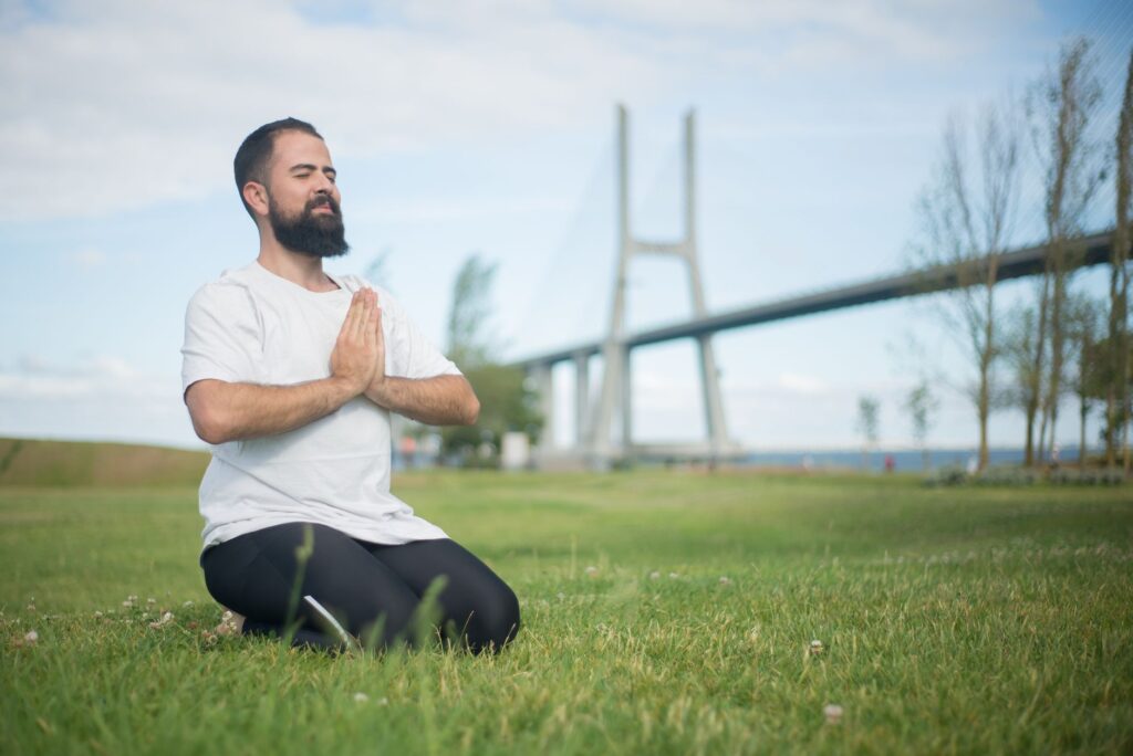 Man practicing meditation on green grass near a bridge in Portugal.