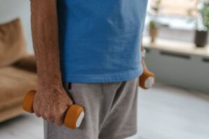 A senior holding orange dumbbells, indoors in casual exercise attire.