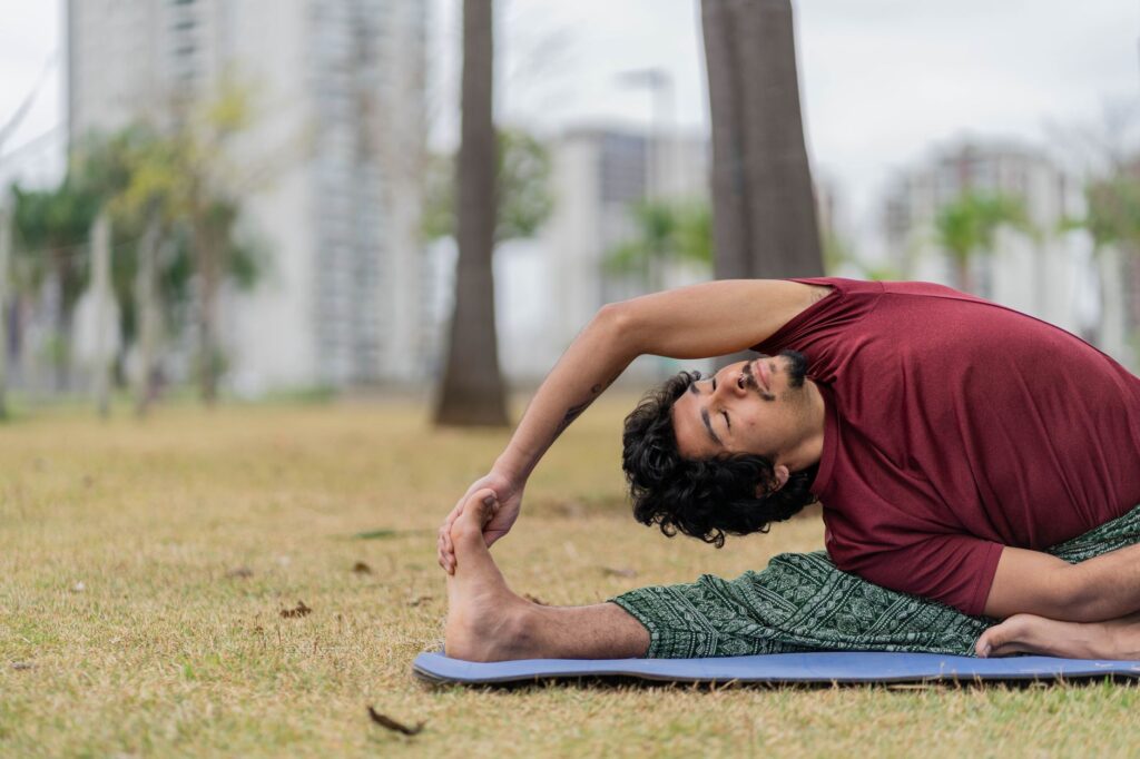 Adult man practicing yoga outdoors in a city park on a mat, showing wellness and flexibility.