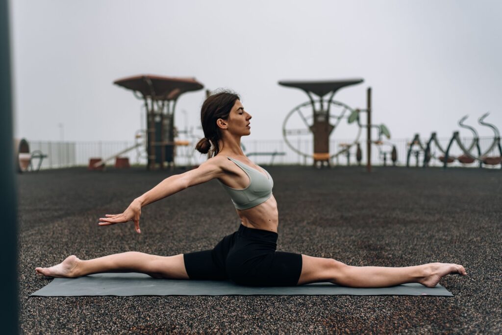 A woman performing yoga splits on a mat outdoors, promoting fitness and flexibility.