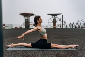A woman performing yoga splits on a mat outdoors, promoting fitness and flexibility.