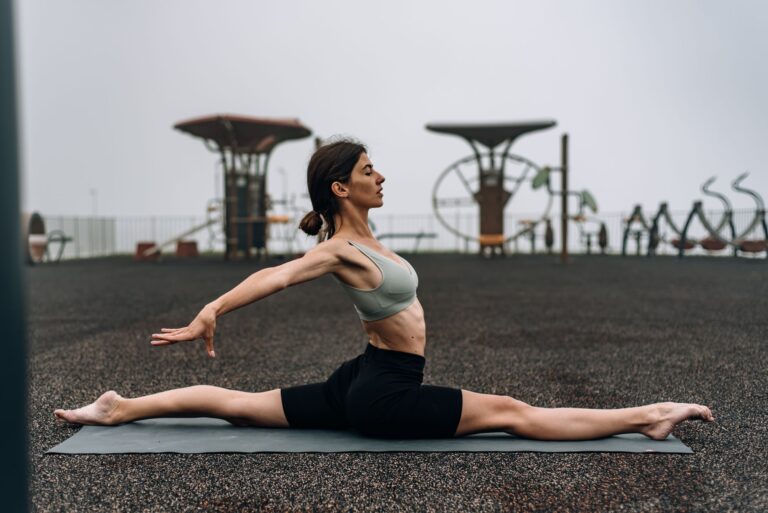 A woman performing yoga splits on a mat outdoors, promoting fitness and flexibility.